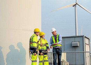 Ein Seniormitarbeiter lehrt zwei Nachwuchsmitarbeitern in einem Windpark an